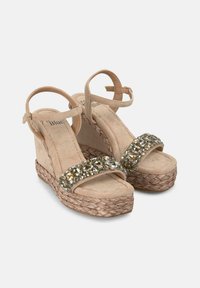 Sandales compensées beige avec une semelle en jute tressé, dotées d'une large sangle ornée de strass et d'une sangle à la cheville réglable. Matériau en daim doux.