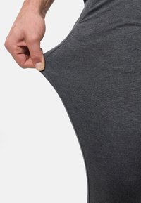 Tejido elástico gris, textura suave, ceñido alrededor de la pierna. Mano tirando del tejido para mostrar flexibilidad. Diseño casual y deportivo.