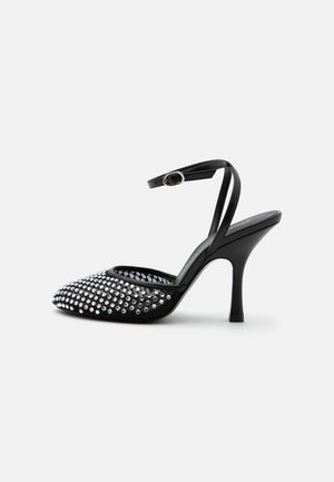 Chaussure noire à talon haut avec bride à la cheville, bout pointu et devant décoré de clous argentés sur une base en mesh transparent.