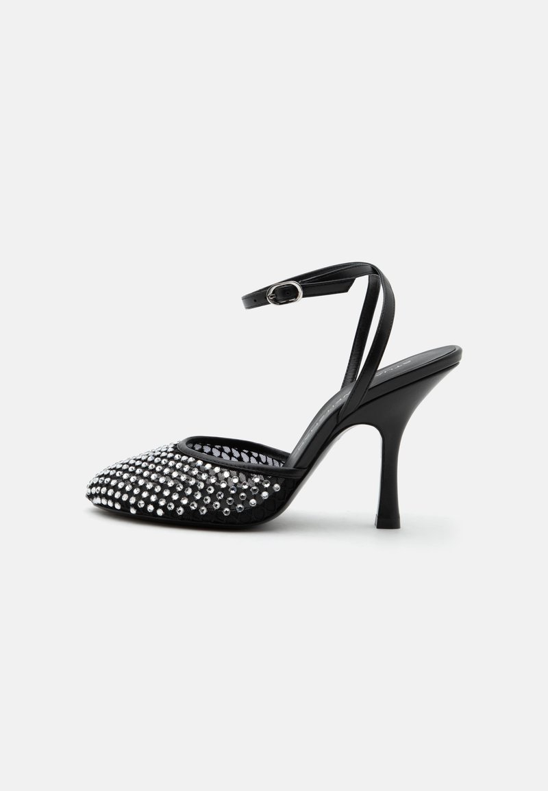 Chaussure noire à talon haut avec bride à la cheville, bout pointu et devant décoré de clous argentés sur une base en mesh transparent.