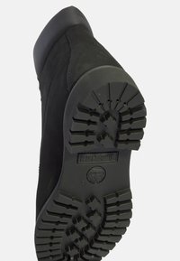 Bota de ante negra con suela de goma que presenta un patrón de relieve profundo. Punta redondeada con un acento negro suave en el borde de la suela.