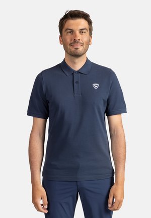 Námořnická modrá polo tričko z jemného materiálu s tříknoflíkovou légou, krátkými rukávy a malým bílým logem na levé hrudi.