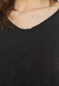 T-shirt noir à col en V avec un col légèrement effiloché et un tissu doux et texturé. Design simple et décontracté.
