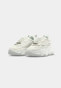 Hvite klumpete sneakers med tykke såler, mesh- og skinnpaneler, snøring foran og trekkinnsats på en ensfarget hvit bakgrunn.