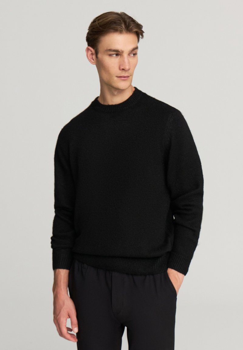 Czarny dzianinowy sweter z okrągłym dekoltem, prążkowanymi mankietami i dolnym obszyciem oraz fakturowanym wykończeniem. Nosi się go na ciemne, casualowe spodnie.