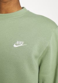 Grön sweatshirt i en bomullsblandning med rund hals och en broderad vit Nike-logotyp på bröstet. Slät textur.