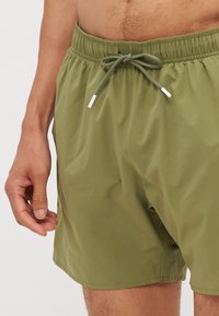 Shorts de bain vert olive en tissu léger et lisse. Dotés d'une taille élastique avec cordon de serrage ajustable et de poches latérales.
