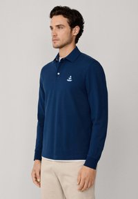 Marineblauwe lange mouw polo shirt van zachte katoen, met een klassieke kraag, een knoopsluiting met drie knopen en een geborduurd logo op de borst.