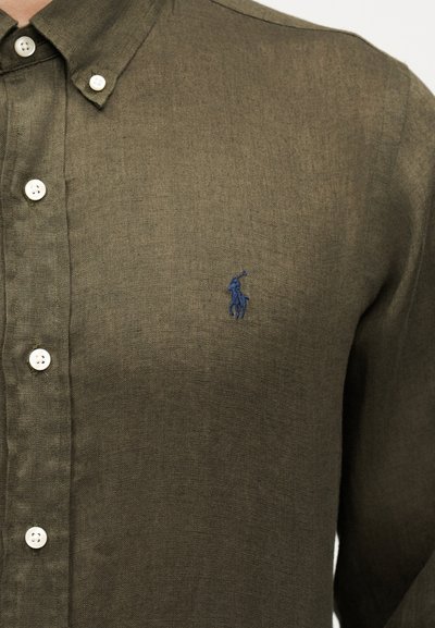 Πουκάμισο χακί με κουμπιά, γιακά και λευκά κουμπιά, με μικρό κέντημα λογότυπο παίκτη πόλο σε ναυτικό μπλε χρώμα στο στήθος.