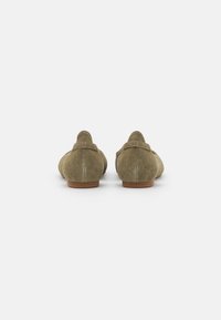 Un paio di scarpe basse in suede verde oliva con suole marroni, viste da dietro su uno sfondo bianco.