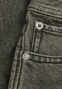 Tamno sivo jeans tkanina s blagom teksturom, koja sadrži metalne zakovice i kontrastne šavove uz rubove džepova.