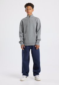 Gray zip-up sweater with a high collar, ribbed hem and cuffs, paired with navy wide-leg pants and white sneakers with black accents.
