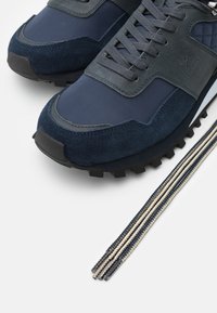 Chaussures de sport bleu marine en suède et mesh, avec des accents texturés, des semelles épaisses en caoutchouc et des lacets contrastants.