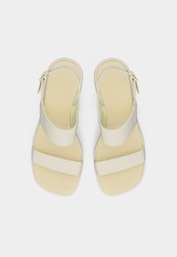 Μπεζ σανδάλια ανοιχτά μπροστά με δύο φαρδιές λουριά και κούμπωμα στον αστράγαλο, σε λευκό φόντο.