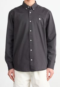 Camicia grigia scuro con bottoni, colletto appuntito, bottoni bianchi e un piccolo logo sul petto a sinistra. Realizzata in tessuto di cotone.