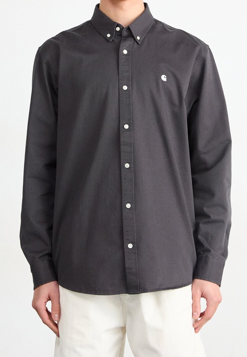 Camicia grigia scuro con bottoni, colletto appuntito, bottoni bianchi e un piccolo logo sul petto a sinistra. Realizzata in tessuto di cotone.