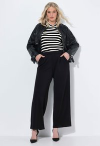Zwarte leren jas over een zwart-witte gestreepte top, gecombineerd met hoog ingezette zwarte wijde broek en zwarte hoge hakken.