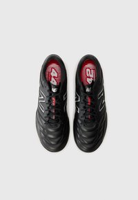 Μαύρα αθλητικά παπούτσια με λείο δερμάτινο επάνω μέρος, με επεξεργασία καπιτονέ, κόκκινες λεπτομέρειες και έντονο ασημένιο λογότυπο "N". Κόκκινη σόλα με μοτίβο.