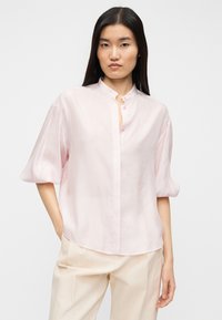 Ανοιχτό ροζ πουκάμισο με κουμπιά, μαο γιακά και κοντά μανίκια με φουσκωτό σχέδιο. Διαθέτει διακριτικό υφασμάτινο μοτίβο και άνετη εφαρμογή.