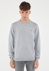 Maglione grigio realizzato in tessuto a maglia morbido, dotato di scollatura rotonda, maniche lunghe e un piccolo logo sul petto. Vestibilità casual.