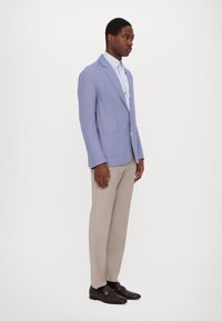 Light purple blazer with notch lapels, two front pockets, worn over a light blue shirt, paired with light gray trousers and dark loafers.