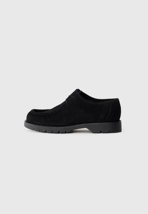 Scarpa in suede nera con punta arrotondata, superficie texture e suola in gomma. Presenta dettagli cuciti e accenti sui pannelli laterali.