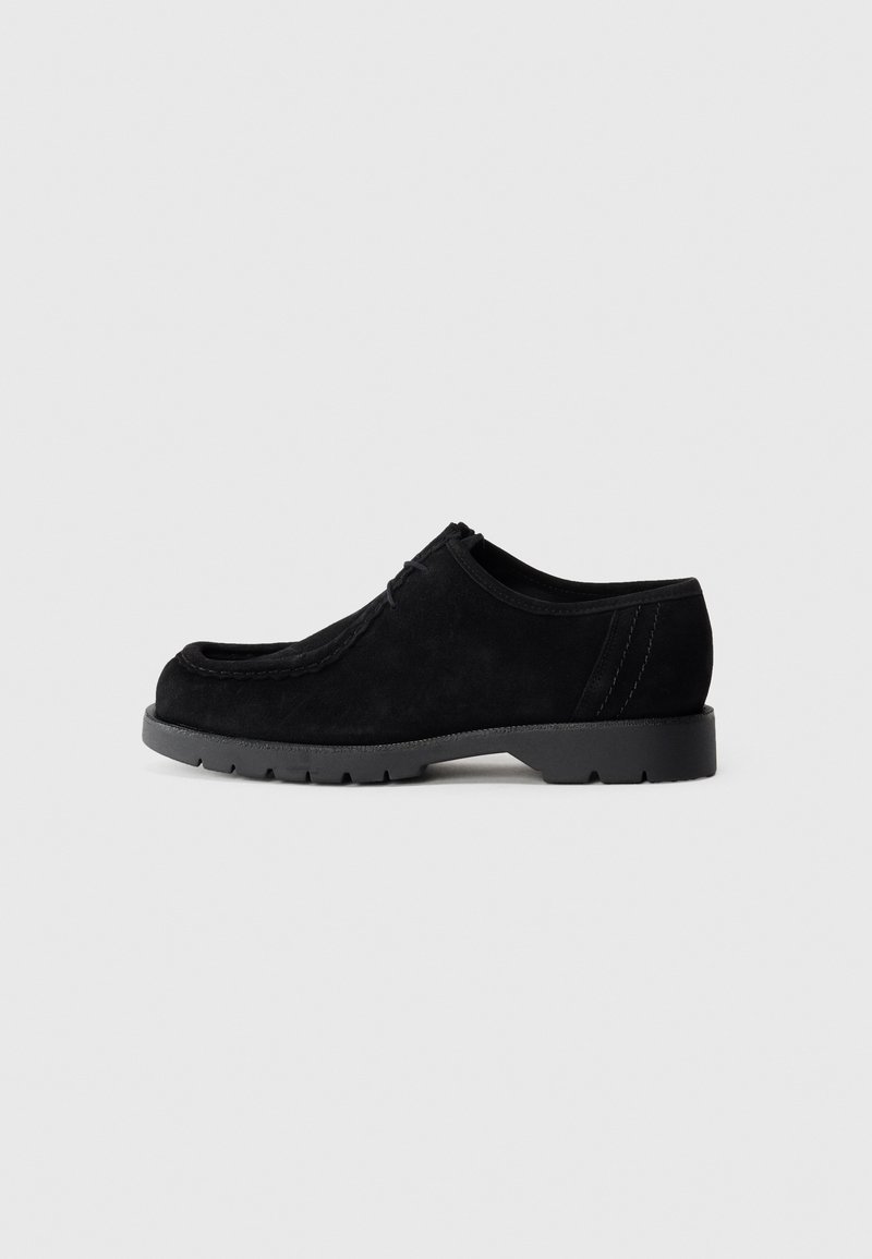 Chaussure en daim noir avec un avant arrondi, surface texturée et semelle en caoutchouc. Présente des détails cousus et des accents sur les panneaux latéraux.
