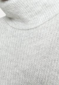 Maglione a collo alto grigio chiaro con texture a coste, materiale morbido e design aderente, che mette in risalto l'area del collo.