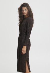 Abito nero con strisce verticali metalliche, maniche lunghe, vita con cintura e spacco laterale, realizzato in un tessuto a maglia testurizzato.