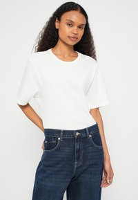 T-shirt branca de manga curta, corte descontraído, material de algodão macio. Combinada com jeans azul escuro de cintura alta, com bolsos frontais e fecho de botão.