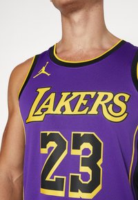 Violet koripallopaita, jossa on keltainen "LAKERS" -teksti ja numero "23", mustalla reunuksella ja Jumpman-logo olkapäässä.