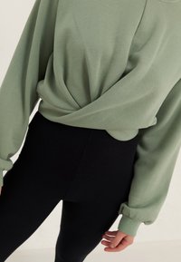 Top holgado de color verde oliva con diseño delantero anudado; combinado con leggings negros acanalados de talle alto.