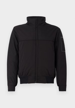 Veste noire avec un col haut, un panneau supérieur contrastant, des poignets et un ourlet élastiques, et une poche zippée sur la manche. Texture de tissu lisse.