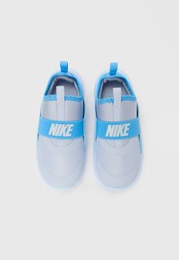 Světlé modré slip-on tenisky Nike s širokými elastickými pásky a poutky, zobrazené z horního pohledu na bílém pozadí.