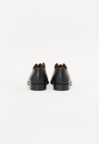 Black leather shoes with a sleek design, featuring low heels and a smooth texture. The back has a rounded cutout detail.