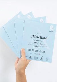 Fem ljusblå ansiktsmaskpaket märkta "STARSKIN" hållna i en hand, med vitt text och en minimalistisk design.
