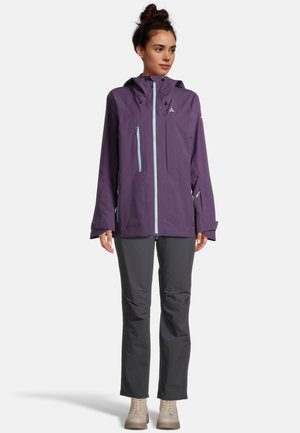 Paarse waterdichte jas met een capuchon, voorzien van lichtblauwe ritsen en meerdere zakken; gecombineerd met grijze broek en beige laarzen.