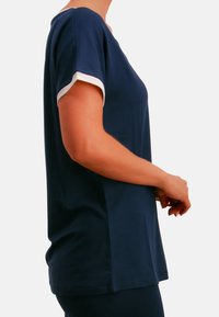 Marineblaues Kurzarm-Oberteil mit weißen Bündchen, rundem Ausschnitt und glattem Stoff. Lockere Passform mit seitlichem Schlitzdetail.