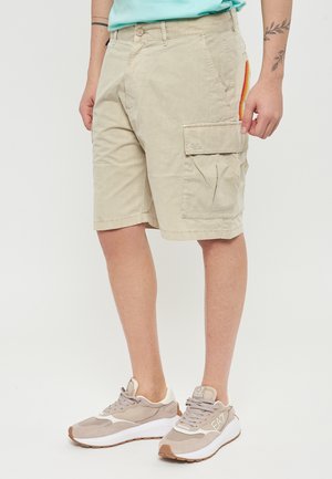 Pantaloni corti beige in stile cargo con una tasca laterale e dettagli a righe multicolori. Realizzati in tessuto morbido con una vestibilità comoda, abbinati a sneakers leggere.