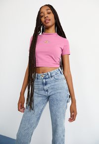 Rosa, kort t-skjorte med rund hals og liten logo. Brukt sammen med høyhåndte lyseblå jeans med en falmet vask og rette ben.