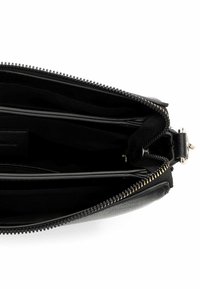 Wnętrze czarnej skórzanej torebki na zamek błyskawiczny, charakteryzujące się gładką fakturą, wieloma przegródkami oraz złotym suwakiem w odcieniu złota.