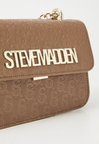 Hnědá kabelka z faux kůže s embosovaným vzorem loga, zlatými kovovými doplňky a výrazn�ým logem "STEVE MADDEN" na předním klopě.