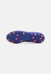 Suela de botas de fútbol moradas con tacos hexagonales y circulares en rosa y azul. Superficie texturizada y detalle del logo de la marca en el costado.
