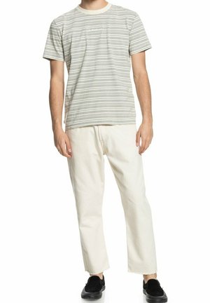 Gestreiftes T-Shirt in Hellgrau und Creme mit kurzen Ärmeln, kombiniert mit hellbeigen Hosen. Die Person trägt schwarze Schuhe.