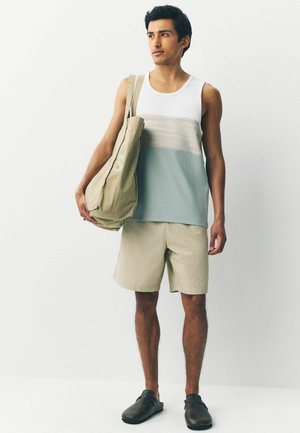Top ligero de tirantes con un diseño de bloques de color blanco, gris y verde azulado, combinado con pantalones cortos beiges y zuecos marrones. Modelo lleva un bolso beige.