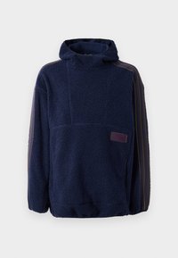 Pulôver de fleece em azul marinho com gola alta e capuz, apresentando um tecido texturizado, etiqueta roxa e detalhes em riscas contrastantes nas mangas.