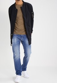 Chaqueta bomber azul marino con un acabado suave, camiseta beige, jeans claros rasgados y zapatillas blancas. La chaqueta cuenta con un bolsillo con cremallera.