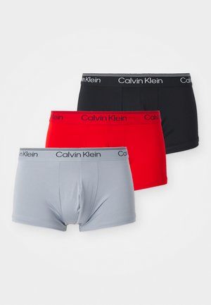 Trois paires de boxers de la marque Calvin Klein en gris, rouge et noir. Chacune dispose d'une taille douce avec le nom de la marque en couleur contrastante.