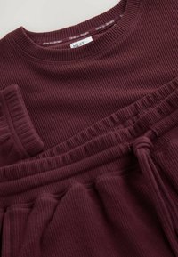 Burgundy loungewear set featuring ribbed texture. Top has a crew neckline; bottom has an elastic waistband and tie detail.