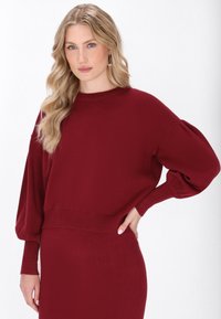 Burgunderfarbener Strickpullover mit kastigem Schnitt, senkten Schultern und gerippten Bündchen. Weiche Textur mit einem einfachen, klaren Design.